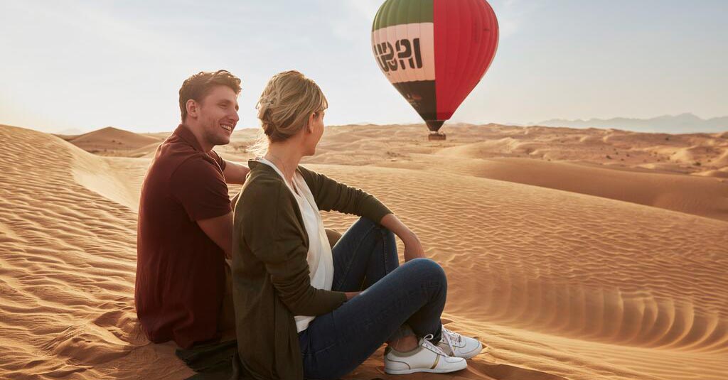 A couple sitting in Dubai desert looking out at a hot air balloon raising into the sky