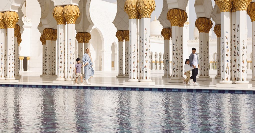 A family walking around Sheikh Zayed Grand Mosque showing the waters and columns