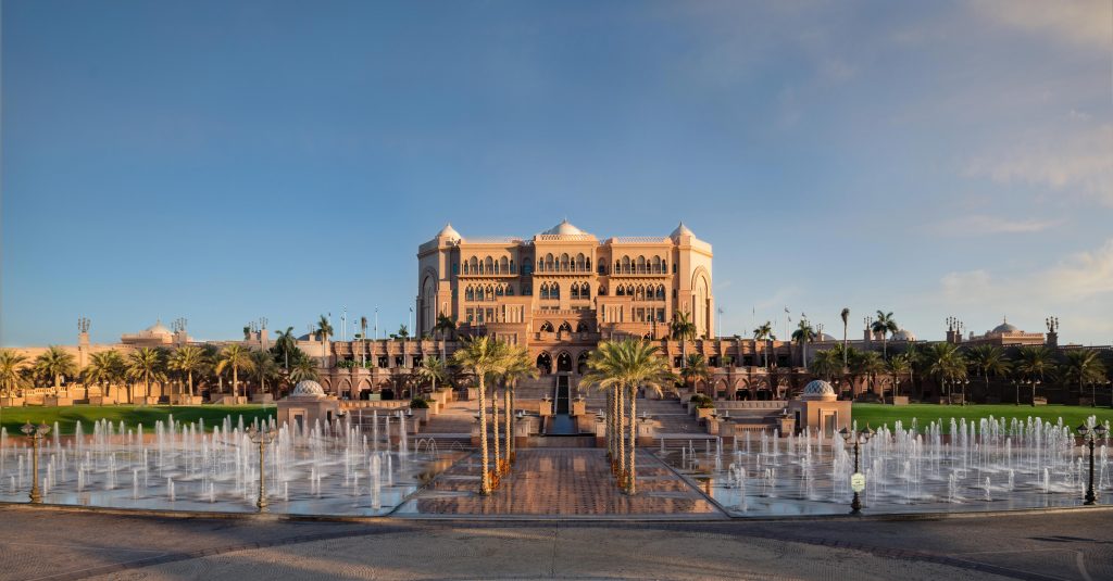 An exterior landscape shot of Emirates Palace Abu Dhabi displaying the fountains and palm trees leading up to the grand entrance