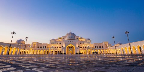 An exterior landscape shot of Qasr Al Watan Palace during sunset as the Palace is illuminated by bright yellow lights.