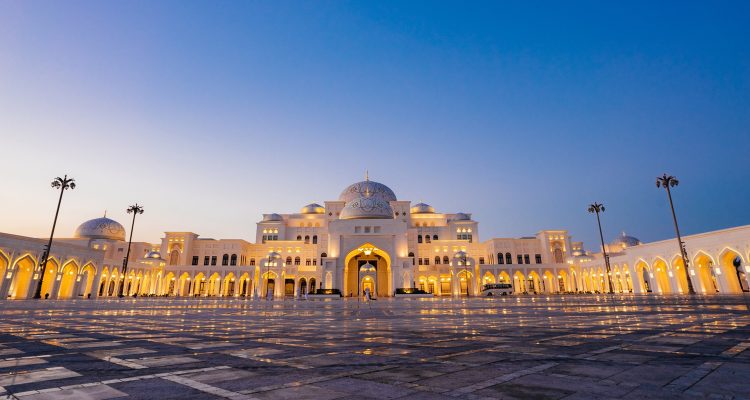 An exterior landscape shot of Qasr Al Watan Palace during sunset as the Palace is illuminated by bright yellow lights.