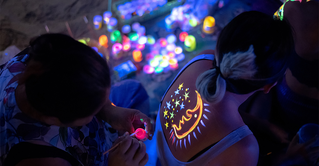 A girl having her back painted in UV paint at the full moon party