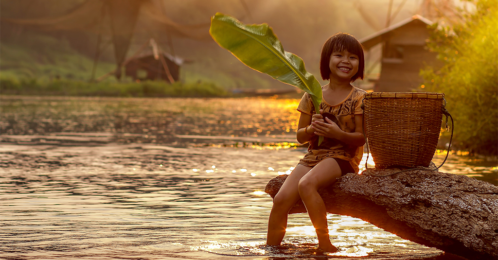 A little Thai girl smiling and dipping her legs into a river
