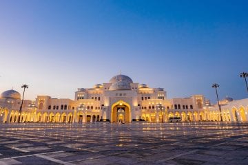 An exterior landscape shot of Qasr Al Watan Palace during sunset as the Palace is illuminated by bright yellow lights.
