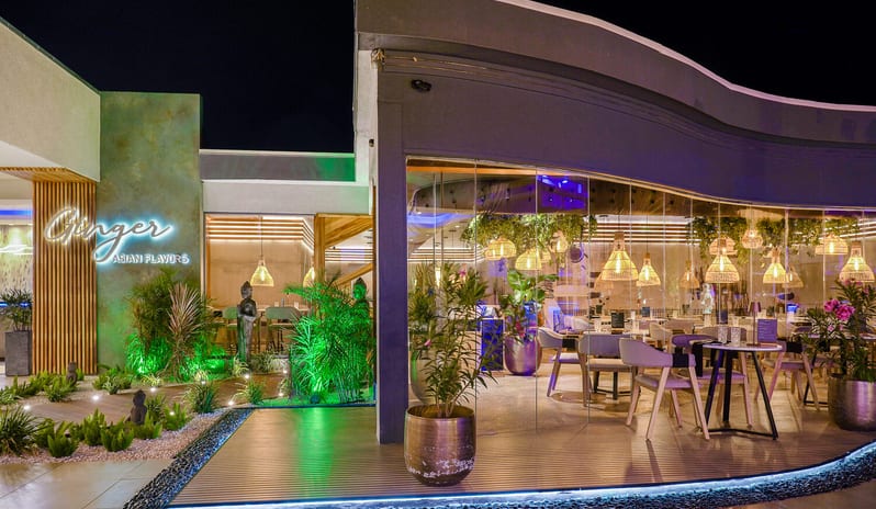 Ginger, Asian Flavors restaurant at dusk, featuring warm ambient lighting, floor-to-ceiling glass walls at Divi Aruba All Inclusive Resort by Kenwood Travel