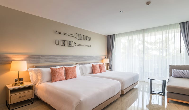 Deluxe Room featuring two twin beds with orange accent pillows, nautical oar wall art, a private balcony with sheer curtains, and a contemporary seating area at Centara Ao Nang Beach Resort & Spa Krabi by Kenwood Travel