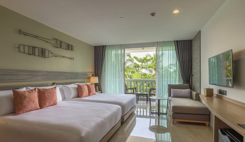 Deluxe Room featuring two twin beds with orange accent pillows, nautical oar wall art, a private balcony with sheer curtains, and a contemporary seating area at Centara Ao Nang Beach Resort & Spa Krabi by Kenwood Travel
