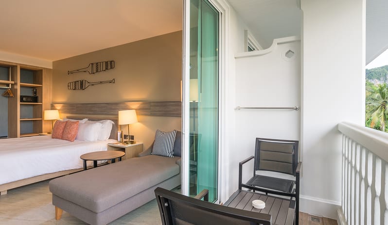 Deluxe Roomshowing a light wood shelving unit with a kettle and coffee tray, a wall-mounted TV, a small refrigerator, and a gray chaise lounge by a large window at Centara Ao Nang Beach Resort & Spa Krabi by Kenwood Travel