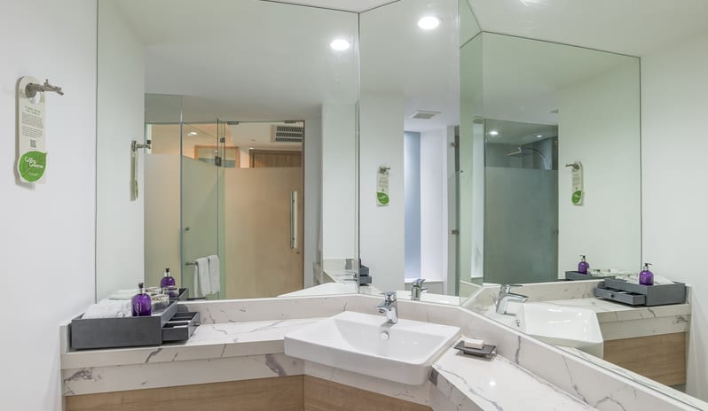 Deluxe Room bathroom featuring a white marble corner vanity with a modern vessel sink, a large wrap-around mirror reflecting a glass at Centara Ao Nang Beach Resort & Spa Krabi by Kenwood Travel