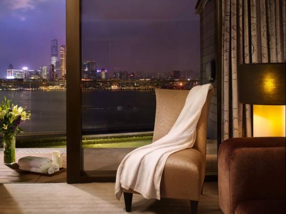 Premier Harbourview Club Room modern sofa, king bed, and a large window overlooking Victoria Harbour and the city skyline at Harbour Grand Hong Kong by Kenwood Travel