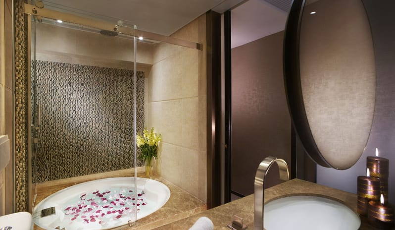 Premier Harbourview Club Room bathroom at Harbour Grand Hong Kong featuring a circular sunken bathtub filled with rose petals, mosaic tile accents, a marble vanity, and ambient candlelight at Harbour Grand Hong Kong by Kenwood Travel