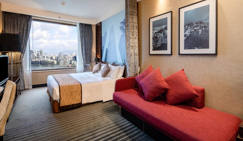 Premier Harbourview Club Room king-sized bed, a large red daybed sofa, and a floor-to-ceiling window offering panoramic views of Victoria Harbourat Harbour Grand Hong Kong by Kenwood Travel