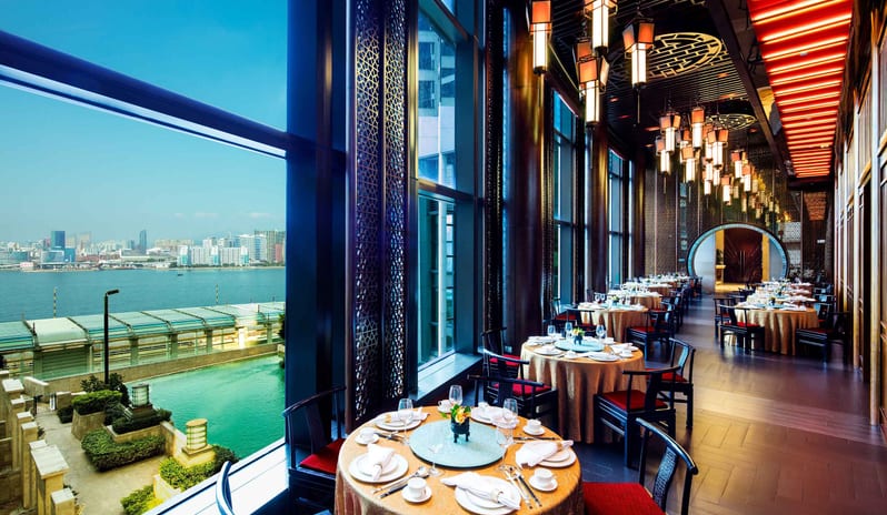 Kwan Cheuk Heen Taditional Chinese decor, round dining tables with gold linens, and large windows overlooking Victoria Harbour at Harbour Grand Hong Kong by Kenwood Travel