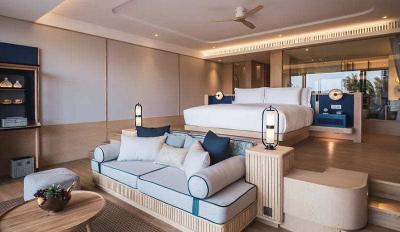 Deluxe Garden Access Suite sunken living area with a grey sofa and an elevated king-size bed overlooking a glass-walled bathroom at Anantara Koh Yao Yai Resort & Villas by Kenwood Travel