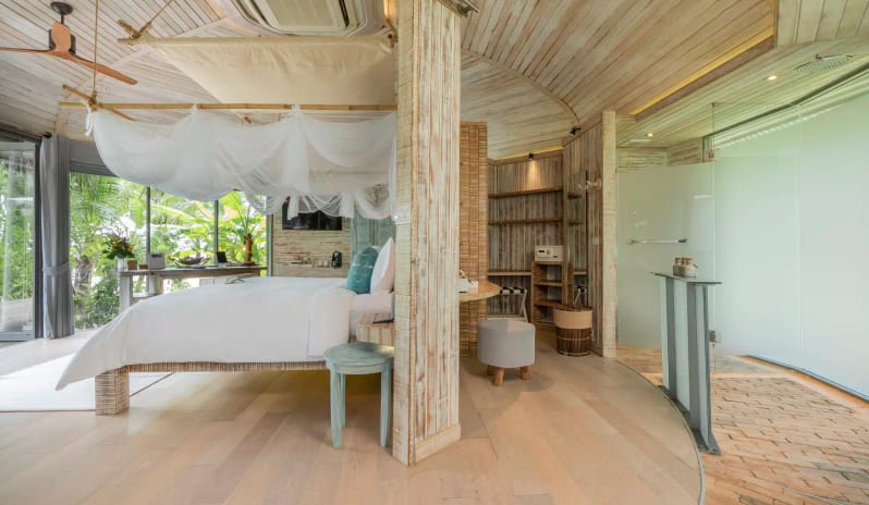 Beachfront Villa Master Bedroom with White Canopy Bed, Rustic Wood Furniture, and Glass Doors Opening to a Private Pool at TreeHouse Villas Koh Yao by Kenwood Travel