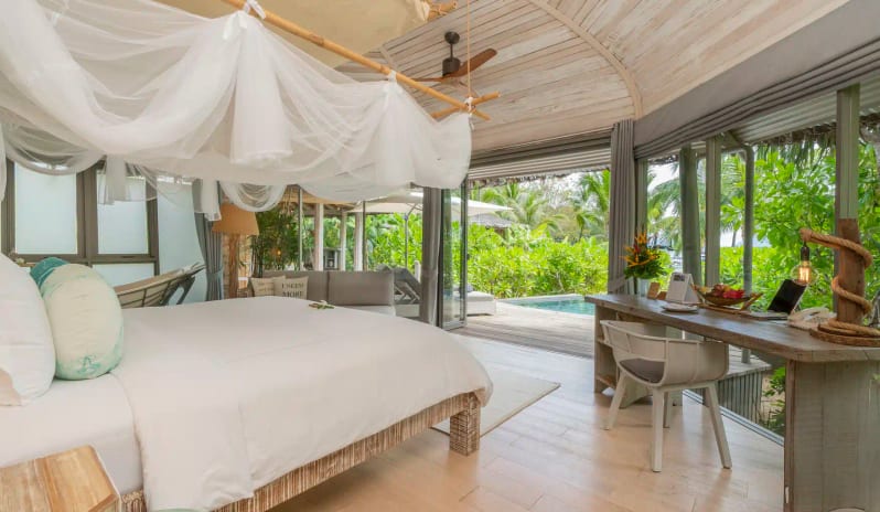 Beachfront Villa Master Bedroom with White Canopy Bed, Rustic Wood Furniture, and Glass Doors Opening to a Private Pool at TreeHouse Villas Koh Yao by Kenwood Travel