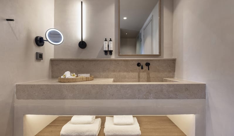 Tropical Bungalow Suite Minimalist tropical bathroom featuring a custom beige stone integrated sink, matte black wall-mounted faucets, a vertical LED sconce, at Aulūs Lindos Rhodes, Curio Collection by Hilton by Kenwood Travel