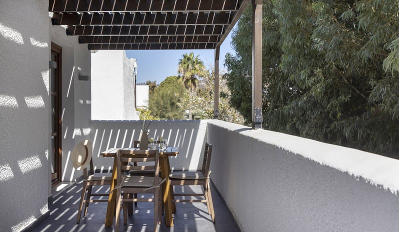 Tropical Bungalow Suite SOutdoor terrace of a tropical suite featuring wooden furniture and white textured walls at Aulūs Lindos Rhodes, Curio Collection by Hilton by Kenwood Travel