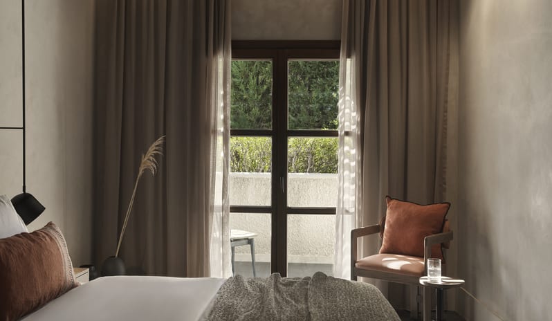 Tropical Cozy Retreat Bedroom with Earth-Toned Bedding, Terracotta Pillows, and Ambient Warm Lighting at Aulūs Lindos Rhodes, Curio Collection by Hilton by Kenwood Travel