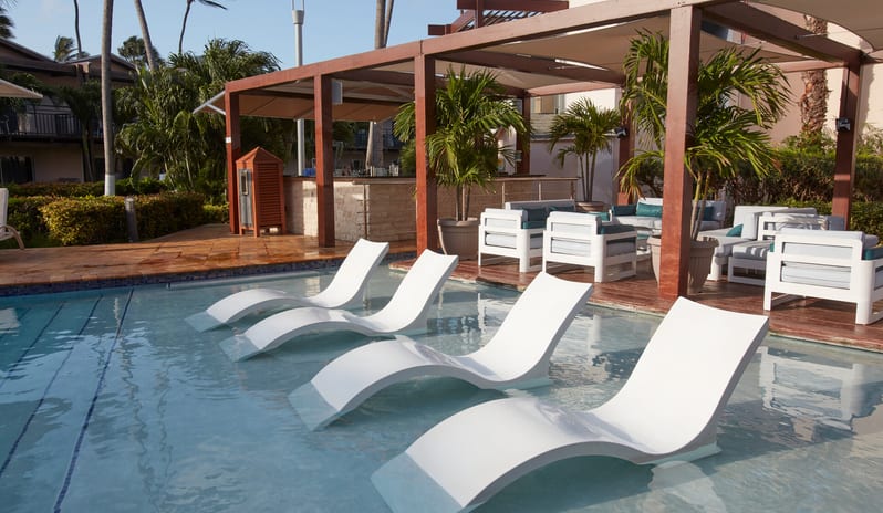 Poolside Bar patio seating area with white furniture and palm trees overlooking a blue resort pool at Divi Aruba All Inclusive Resort by Kenwood Travel