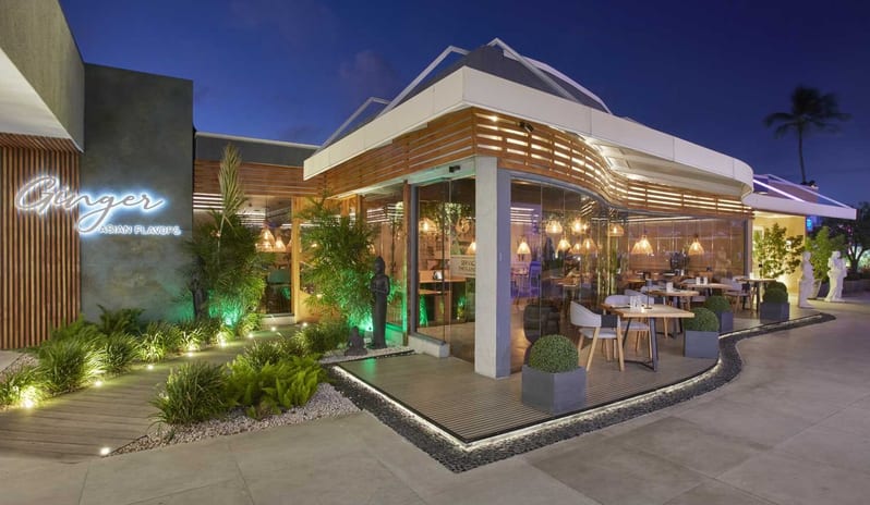 Ginger, Asian Flavors restaurant at dusk, featuring warm ambient lighting, floor-to-ceiling glass walls at Divi Aruba All Inclusive Resort by Kenwood Travel