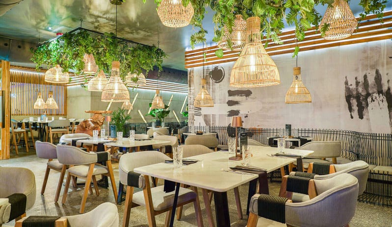 Ginger, Asian Flavors restaurant at dusk, featuring warm ambient lighting, floor-to-ceiling glass walls at Divi Aruba All Inclusive Resort by Kenwood Travel