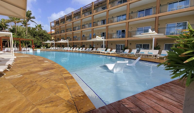Pool View Room King wooden sun deck with private cabanas, palm trees, and a shallow lounge pool overlooking the ocean at sunset at sunsetl at Divi Aruba All Inclusive Resort by Kenwood Travel