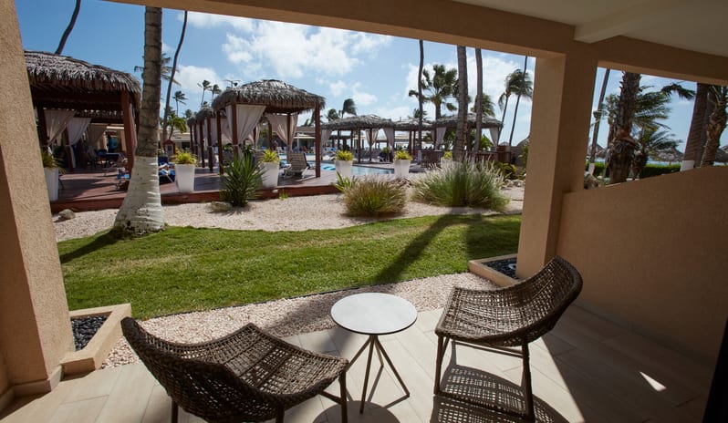 Pool View Room Queen QueenAn aerial perspective of a tropical resort's wooden sun deck featuring private cabanas, palm trees, and a shallow lounge pool at sunset at Divi Aruba All Inclusive Resort by Kenwood Travel