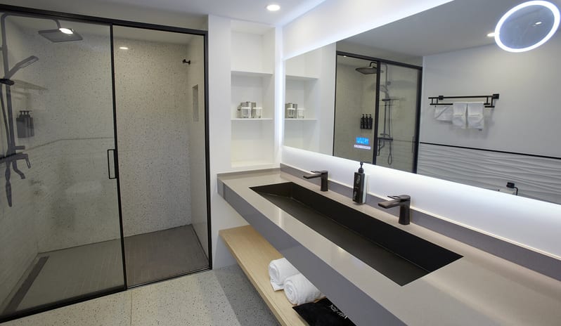 Ocean View Room Queen Queen bathroom featuring a large walk-in glass shower, a long gray vanity with two black faucets, and a backlit LED mirror at Divi Aruba All Inclusive Resort by Kenwood Travel