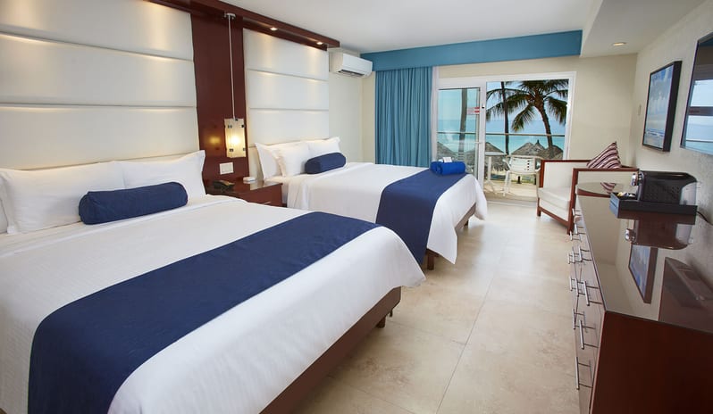 Oceanfront Lanai Room Queen Queen bed with navy accents, a seating area, and sliding glass doors opening to a private terrace with an ocean view at Divi Aruba All Inclusive Resort by Kenwood Travel
