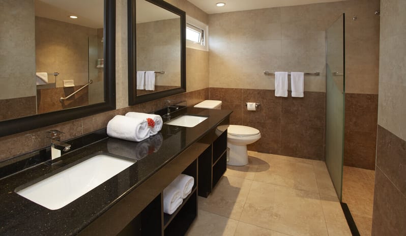 Oceanfront Lanai Room Queen Queen Bathroom double vanity with black granite countertops, large framed mirrors, and a glass-enclosed walk-in shower at Divi Aruba All Inclusive Resort by Kenwood Travel