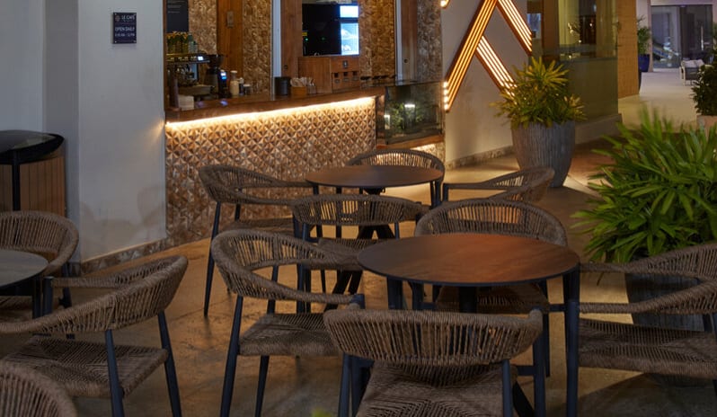 Le Caféat night, featuring a lit pastry display case filled with croissants, an espresso machine, and a patio with wicker chairs under a white sail canopy at Divi Aruba All Inclusive Resort by Kenwood Travel