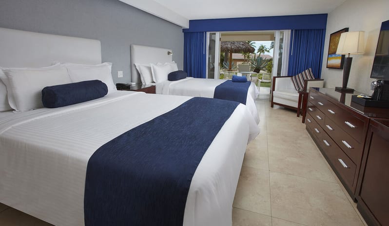 Garden View Room Queen Queen bed with navy blue accents, a minimalist wooden desk, and two blue lounge chairs facing a private outdoor terrace at Divi Aruba All Inclusive Resort by Kenwood Travel