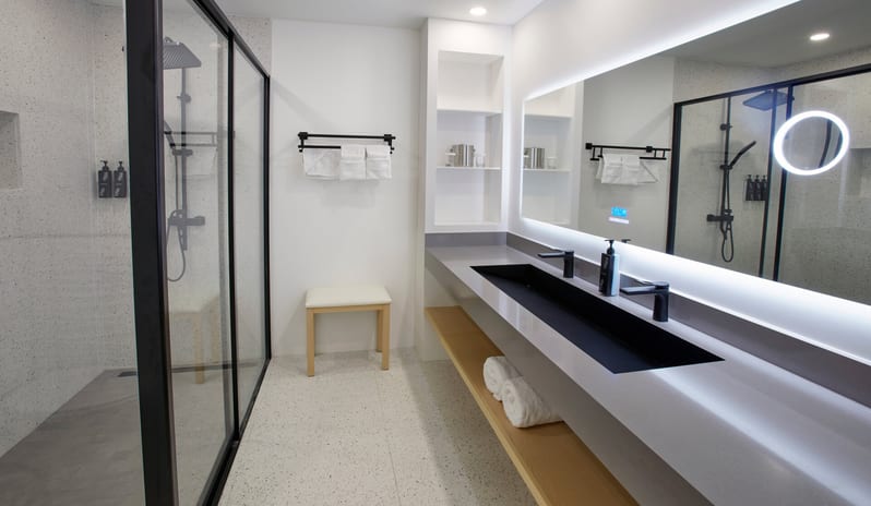 Beachside Room King bathroom featuring a long grey double vanity, a large backlit LED mirror, and a spacious glass-enclosed walk-in shower with black hardware at Divi Aruba All Inclusive Resort by Kenwood Travel