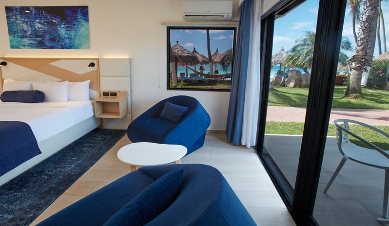 Beachside Room Queen Queen Spacious adjoining hotel rooms featuring a double queen bedroom in the foreground and a king bedroom visible through an open door, both with modern blue decor and garden views at Divi Aruba All Inclusive Resort by Kenwood Travel