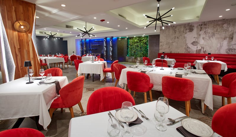 Red Parrot restaurant interior featuring red velvet chairs, white tablecloths, spiky black chandeliers, a blue-lit wine cellar wall, and a vertical green living wall at Divi Aruba All Inclusive Resort by Kenwood Travel