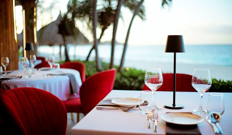 Red Parrot restaurant interior featuring red velvet chairs, white tablecloths, spiky black chandeliers, a blue-lit wine cellar wall, and a vertical green living wall at Divi Aruba All Inclusive Resort by Kenwood Travel