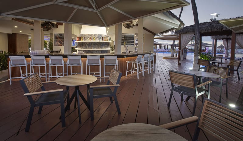 Coco Grill & Bar Modern resort bar with white high-back stools, wood-paneled counter, and a central blue marble pizza oven at Divi Aruba All Inclusive Resort by Kenwood Travel