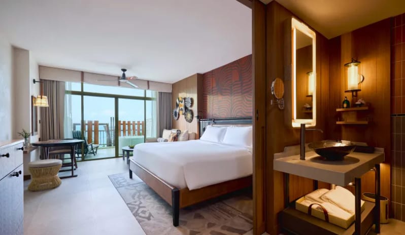 Premium Spa Explorer (King) bed with white linens, a textured orange accent wall, and large sliding glass doors leading to a private balcony with an outdoor spa tub at Centara Grand Mirage Beah Resort by Kenwood Travel