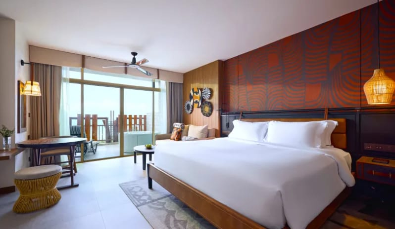 Premium Spa Explorer (King) bed with white linens, a textured orange accent wall, and large sliding glass doors leading to a private balcony with an outdoor spa tub at Centara Grand Mirage Beah Resort by Kenwood Travel