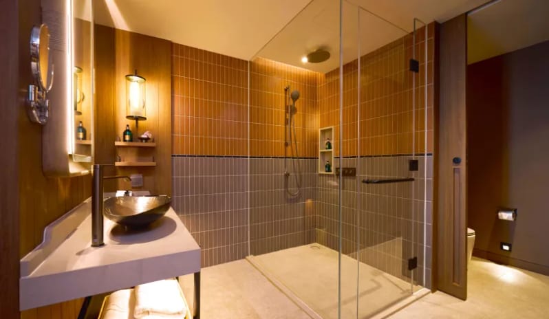 Premium Spa Explorer (King) bathroom featuring a glass-enclosed walk-in rain shower with two-tone vertical tiles, a stone vessel sink, and warm ambient lighting at Centara Grand Mirage Beah Resort by Kenwood Travel