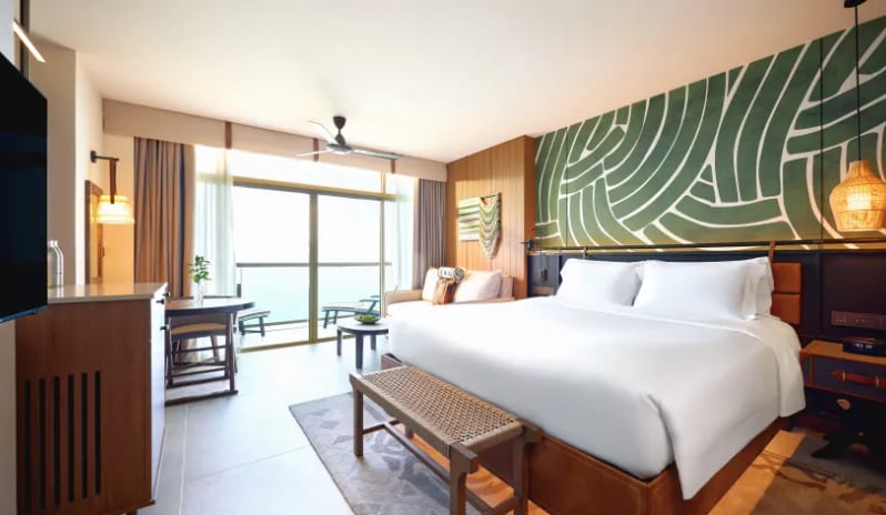 Mirage Premium Explorer (King) bed with white linens, a green abstract mural headboard, and floor-to-ceiling glass doors opening to a private balcony with an ocean view at Centara Grand Mirage Beah Resort by Kenwood Travel