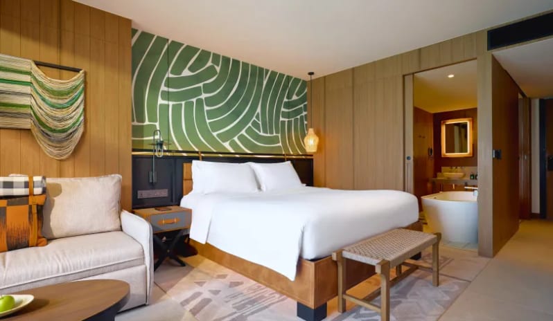 Mirage Premium Explorer (King) bed with white linens, a green abstract mural headboard, and floor-to-ceiling glass doors opening to a private balcony with an ocean view at Centara Grand Mirage Beah Resort by Kenwood Travel