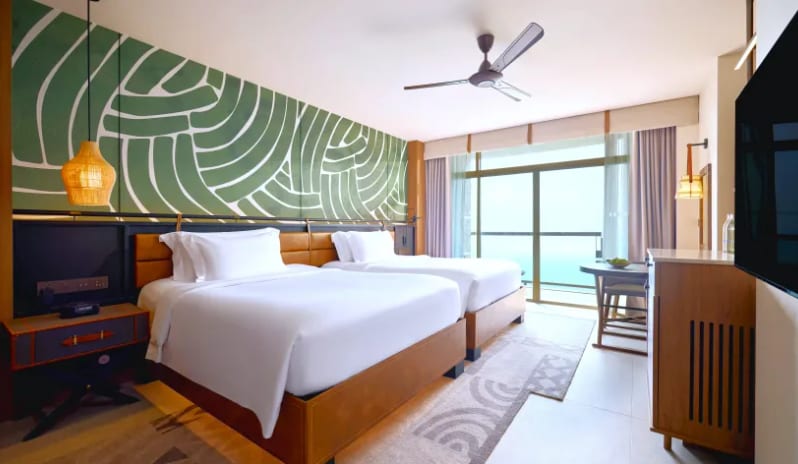 Deluxe Explorer (DBL/DBL) private balcony with ocean views, a large green graphic wall mural, a ceiling fan, and modern wood furnishings with woven pendant lighting at Centara Grand Mirage Beah Resort by Kenwood Travel
