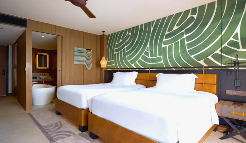 Deluxe Explorer (DBL/DBL) Mirage Premium Explorer (DBL/DBL)twin bedroom at Mirage Premium Explorer featuring a green abstract mural, wood-paneled walls, an open-concept bathroom with a freestanding soaking tub, and contemporary leather headboards at Centara Grand Mirage Beah Resort by Kenwood Travel