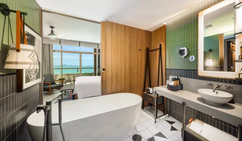 Mirage Suite (King) bathroom featuring a large freestanding white soaking tub, green and gray tiled walls, a vessel sink, and a view into the bedroom toward the sea at Centara Grand Mirage Beah Resort by Kenwood Travel