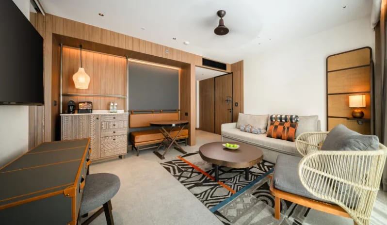 Mirage Suite (DBL/DBL) living room showing a kitchenette area with an espresso machine, leather bench seating, and a large wall-mounted TV at Centara Grand Mirage Beah Resort by Kenwood Travel