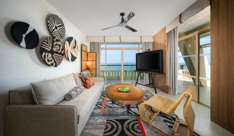 Centara Grand Mirage Beah Resort Mirage Family Suite with Bunk Bed (DBL/DBL) living area in the Mirage Family Expedition Suite with a grey sofa, tribal wall art, a live-edge wooden coffee table, and large sliding doors leading to a balcony with an ocean view-Kenwood Travel-Kenwood Travel