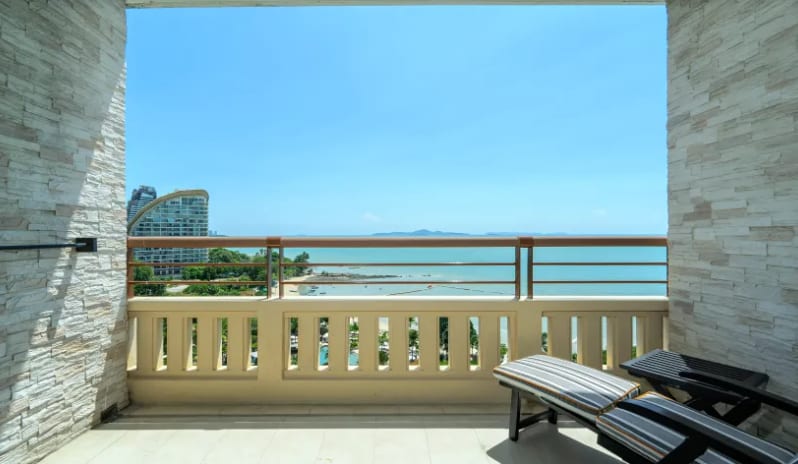 Deluxe Explorer (DBL/DBL) balcony with a scenic sea view, stone textured walls, and comfortable outdoor seating under a clear blue sky at Centara Grand Mirage Beah Resort by Kenwood Travel