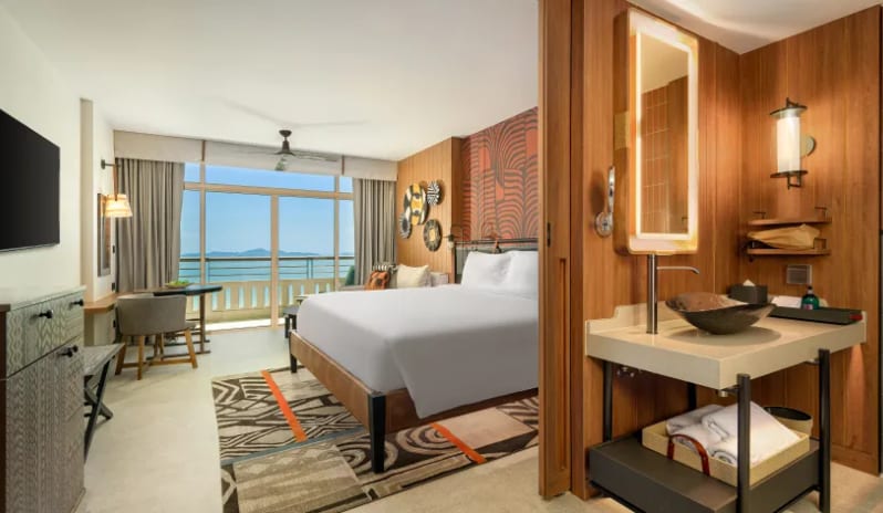 Deluxe Explorer (DBL/DBL) bathroom vanity with a backlit mirror and stone vessel sink, looking through to a bright bedroom with a balcony overlooking the ocean at Centara Grand Mirage Beah Resort by Kenwood Travel